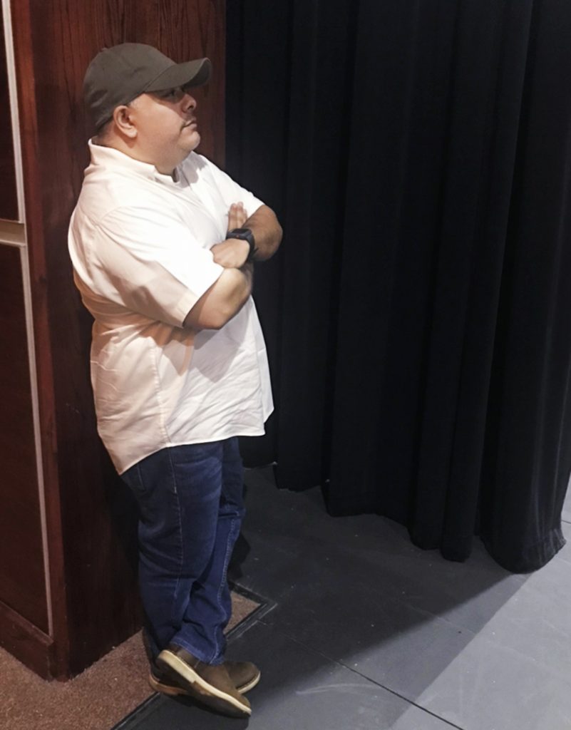 Instructional Associate Professor of theater Gilberto Martinez stands behind the curtain on stage at TAMIU.