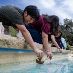 Students put paper boats into the campus fountain.