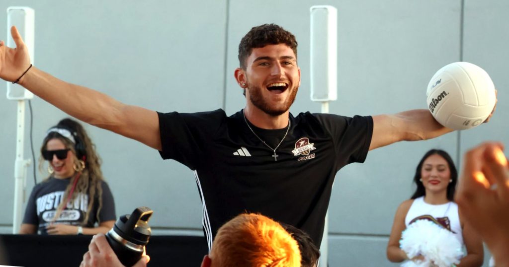 Soccer player holds a soccer ball and puts his arms out to get the crowd to cheer.