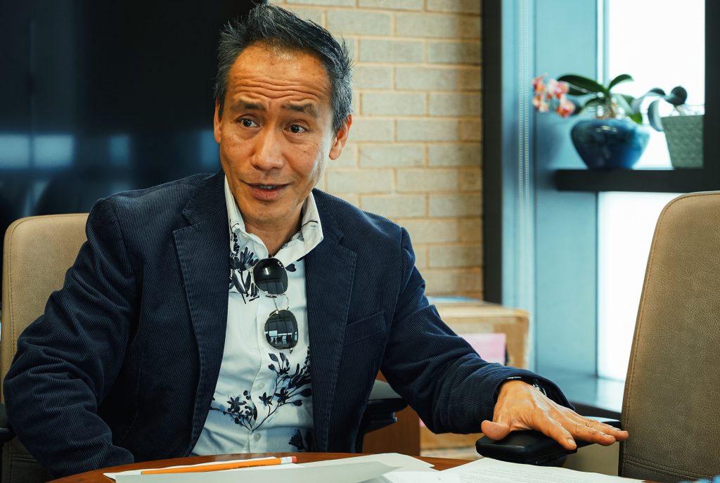 Dean Ynalvez gestures as he speaks at his desk in his office.