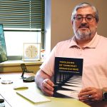 Professor holds book and poses for a portrait.