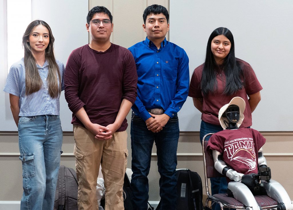 Four engineering students pose for a group photo with a robot.
