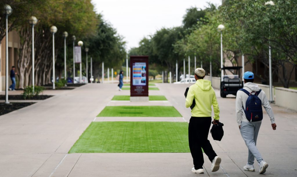 Students walk near the artificial green turf on campus.