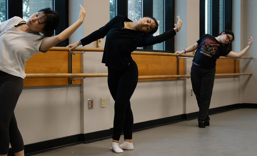 three contemporary dancers practice their form in a classroom