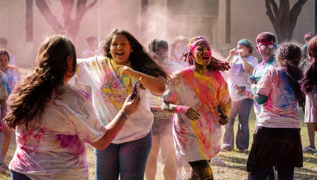 A group of students in white T-shirts throw colored chalk at one another.