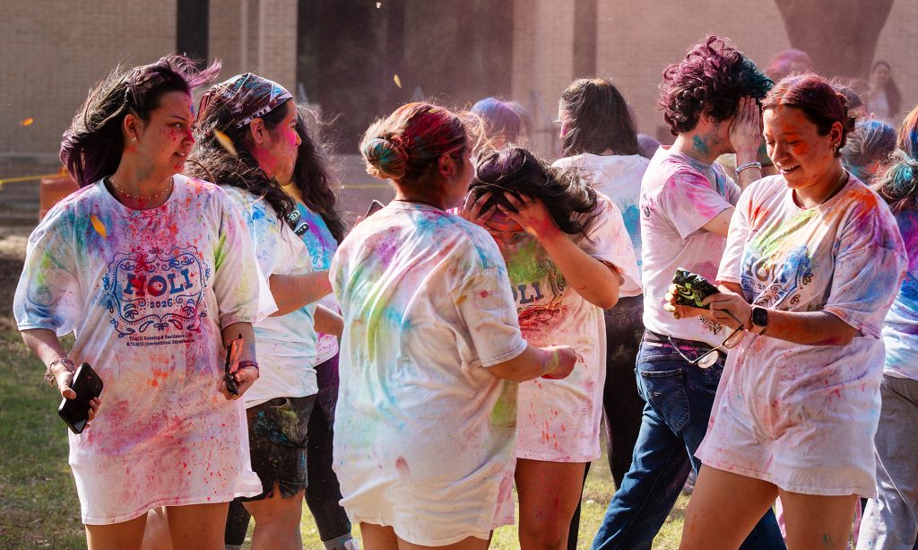 A group of students in white T-shirts throw colored chalk at one another.