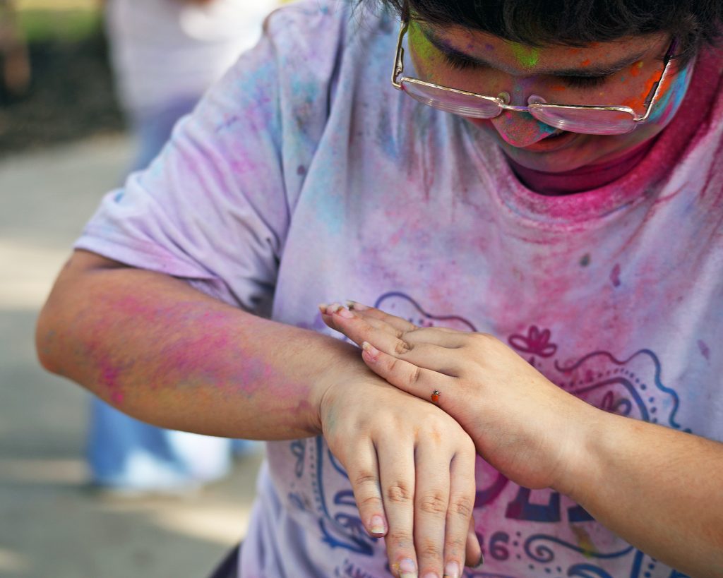 A female student with a white T-shirt covered in colored chalk looks at a ladybug on her wrist.