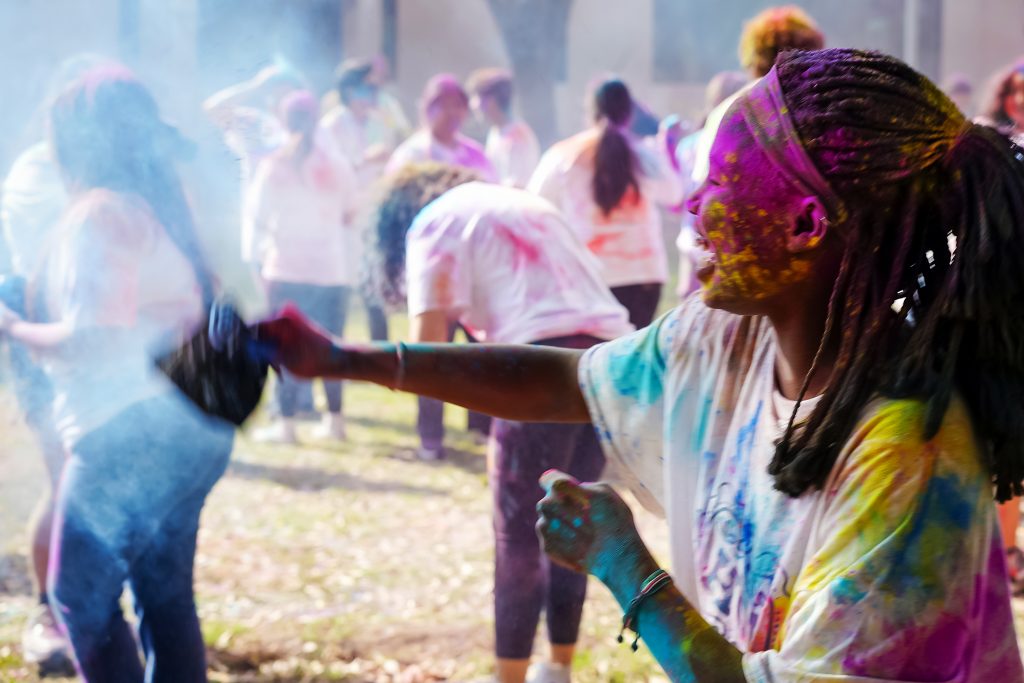 A group of students in white T-shirts throw colored chalk at one another.