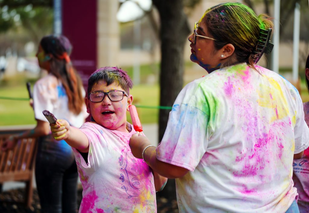 Two people wearing white T-shirts covered in various colors of powder.