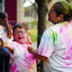 Two people wearing white T-shirts covered in various colors of powder.