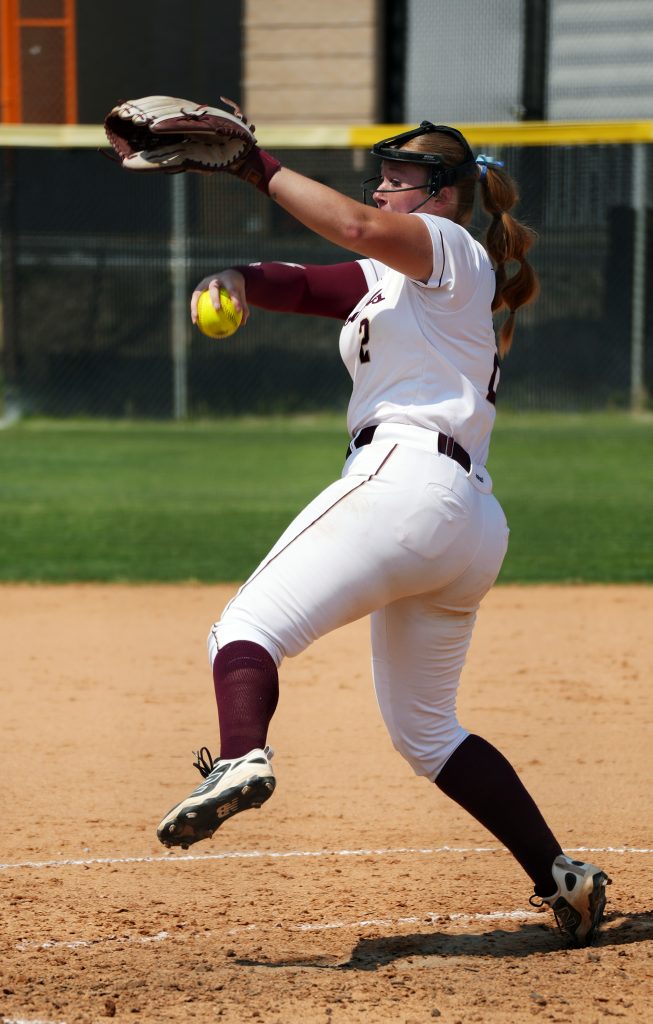 A softball pitcher winds up to throw the ball toward the plate.