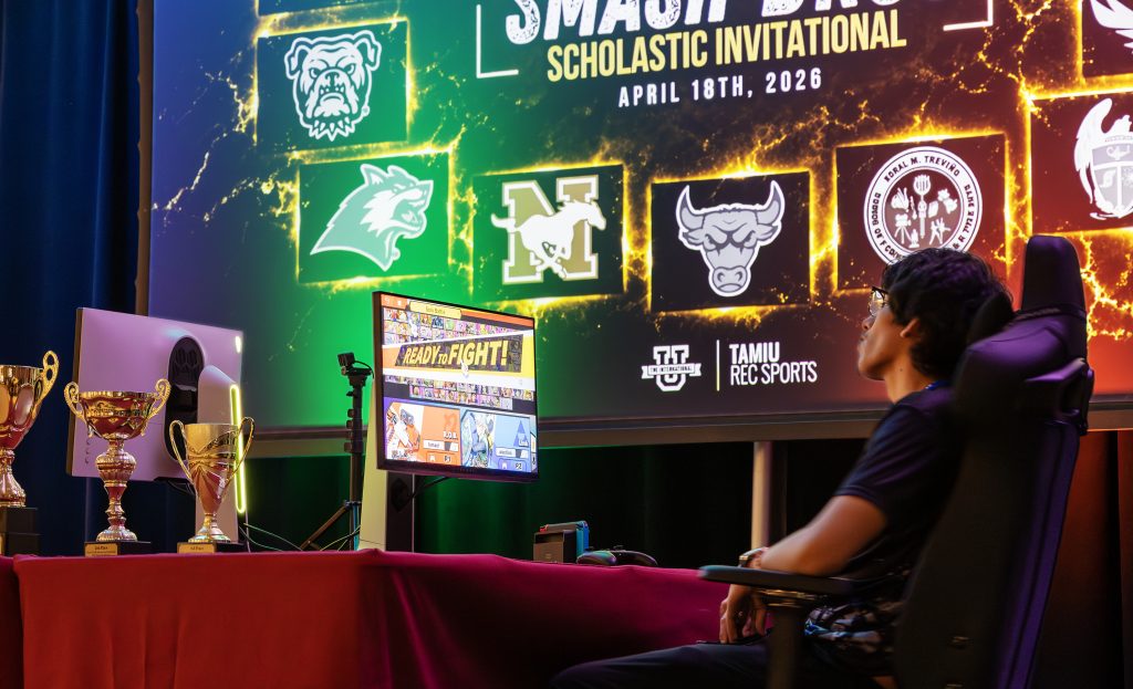 A student plays a video game during an esports event. A large monitor displays the tournament bracketing the background.