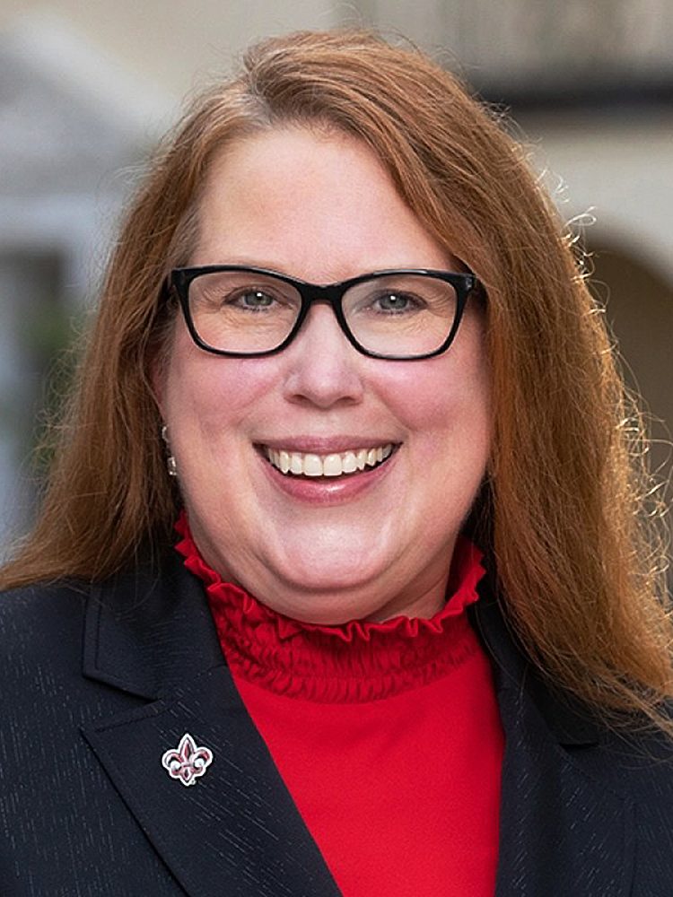 portrait of Amy Armstrong with a black jacket, red shirt, and glasses.
